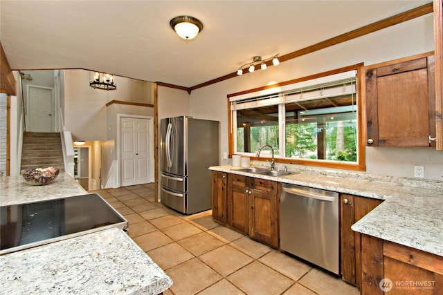 kitchen featuring light tile patterned floors, light stone counters, ornamental molding, stainless steel appliances, and a sink