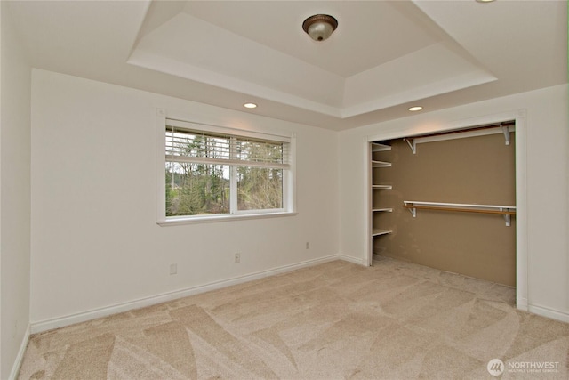 unfurnished bedroom featuring carpet floors, a tray ceiling, a closet, and baseboards