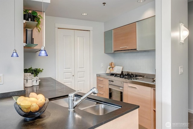 kitchen with dark countertops, oven, a sink, gas cooktop, and backsplash