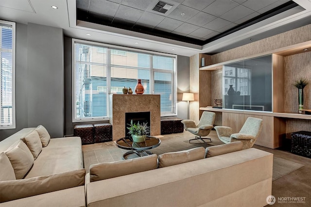 living room with plenty of natural light, a tray ceiling, a tiled fireplace, and visible vents