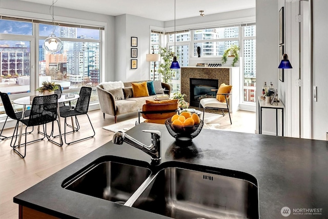 kitchen with decorative light fixtures, dark countertops, a glass covered fireplace, a sink, and wood finished floors