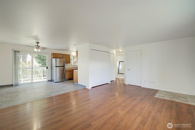 unfurnished living room featuring light wood-type flooring, a sink, baseboards, and ceiling fan