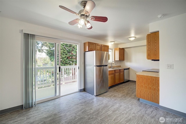 kitchen with stainless steel appliances, a sink, baseboards, light countertops, and brown cabinetry