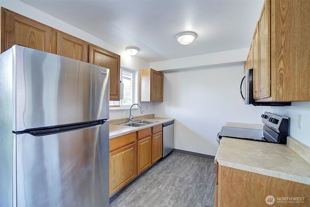 kitchen featuring brown cabinetry, appliances with stainless steel finishes, light countertops, and a sink