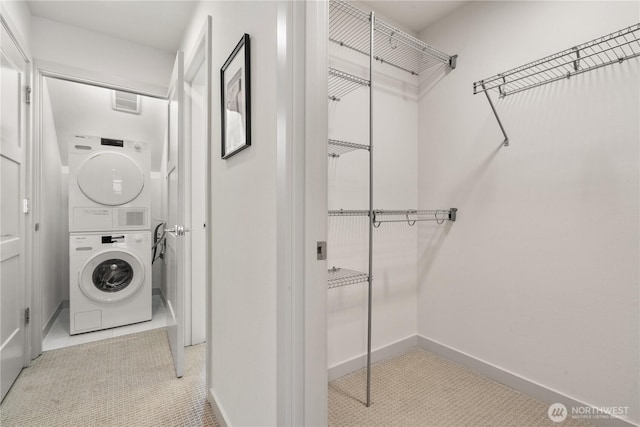 clothes washing area featuring laundry area, stacked washer and clothes dryer, and baseboards