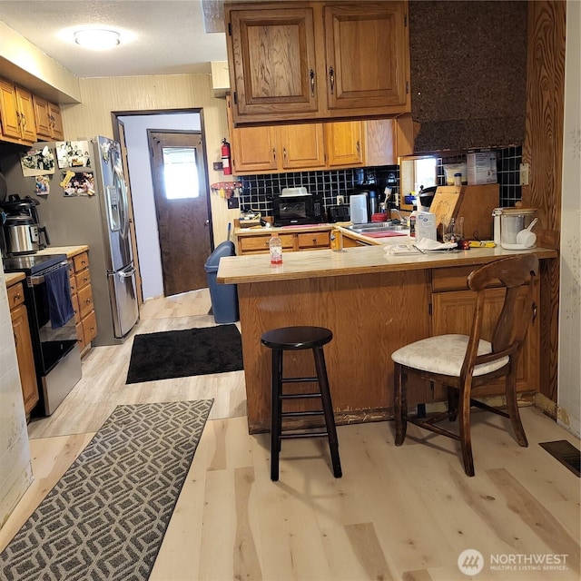 kitchen with a breakfast bar area, light wood-style flooring, a peninsula, electric range, and light countertops