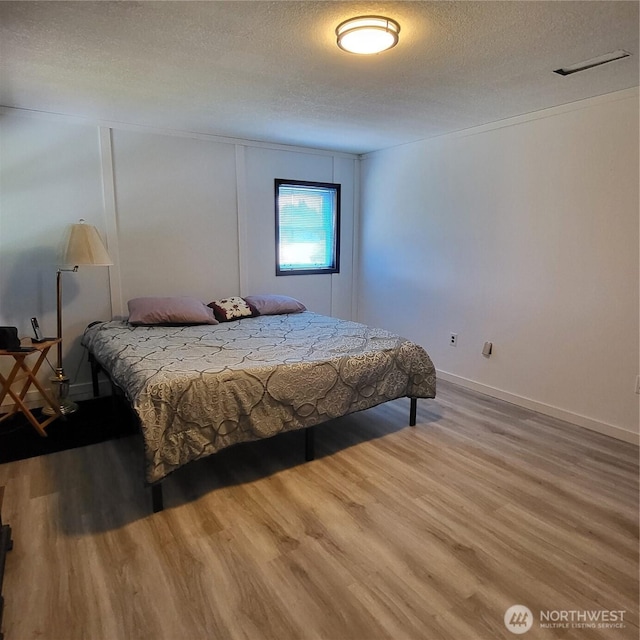 bedroom featuring a textured ceiling, wood finished floors, visible vents, and baseboards