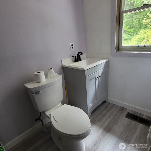 half bath featuring toilet, baseboards, visible vents, and wood finished floors