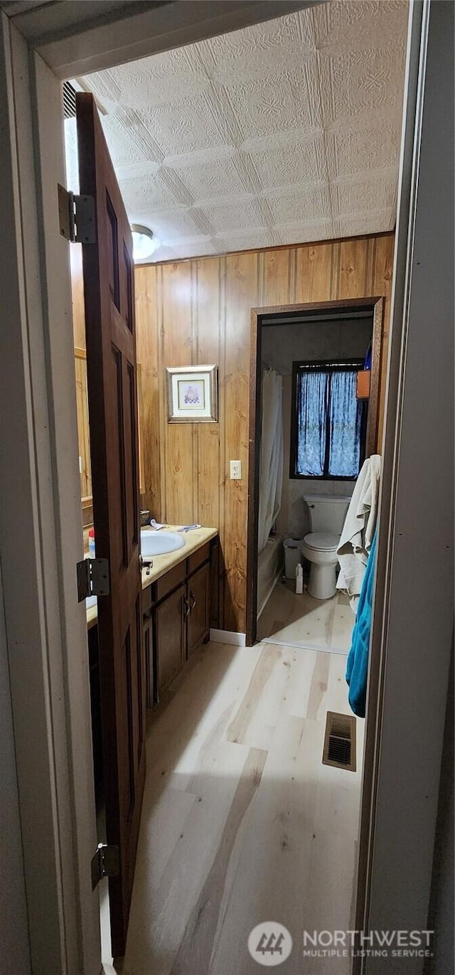 half bath with toilet, wood walls, visible vents, and a sink