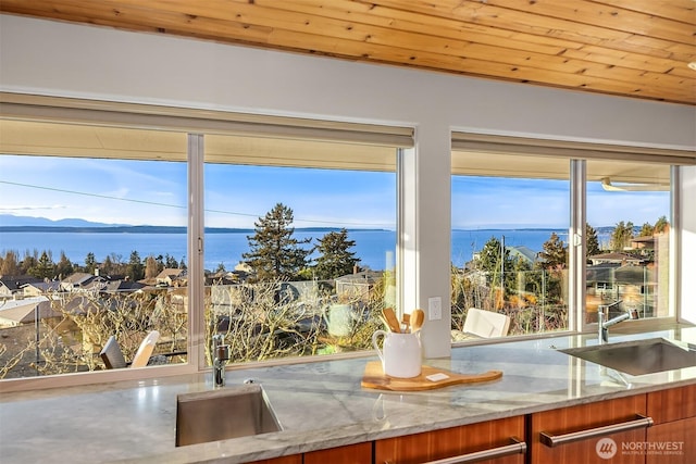 interior space featuring brown cabinetry, wooden ceiling, a sink, and light stone countertops