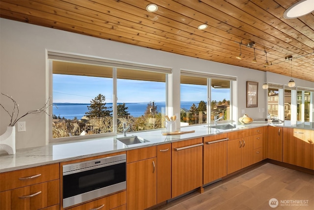 kitchen featuring decorative light fixtures, wood ceiling, a sink, light wood-type flooring, and oven