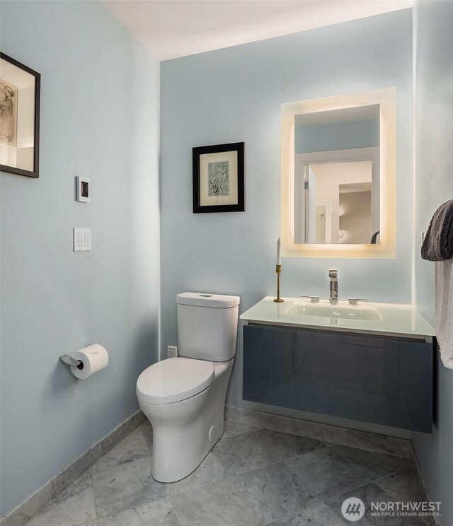 half bath featuring marble finish floor, vanity, toilet, and baseboards