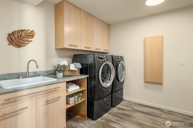 clothes washing area with light wood finished floors, cabinet space, baseboards, washer and dryer, and a sink