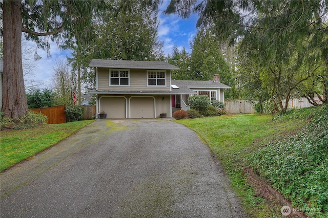 traditional home with driveway, a chimney, an attached garage, fence, and a front lawn