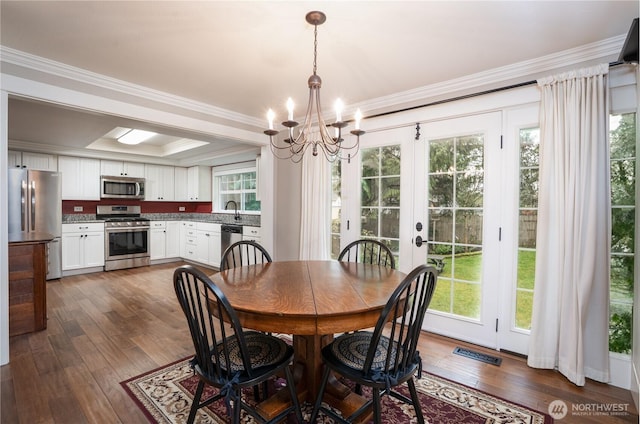 dining space featuring visible vents, a raised ceiling, dark wood-style floors, ornamental molding, and a healthy amount of sunlight