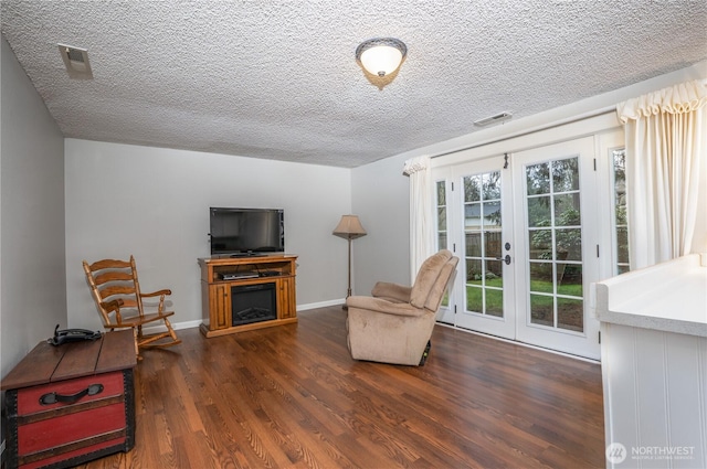 sitting room featuring a textured ceiling, a fireplace, wood finished floors, visible vents, and french doors