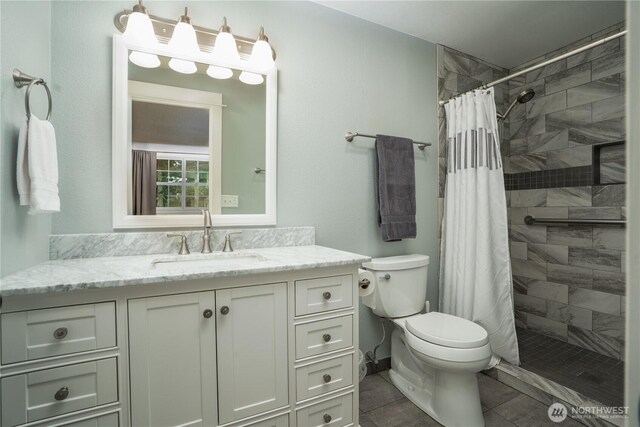 bathroom with toilet, tile patterned floors, tiled shower, and vanity