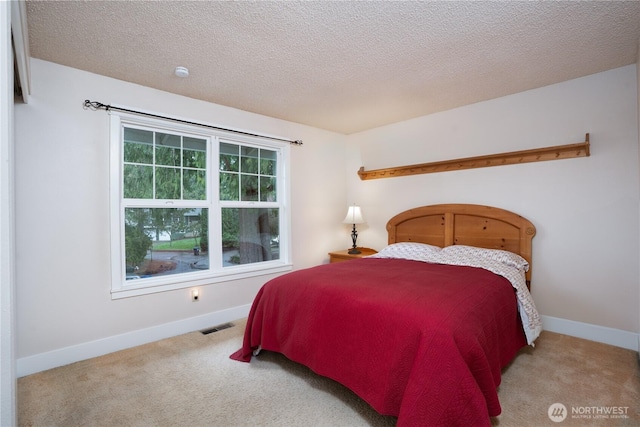 bedroom with baseboards, a textured ceiling, visible vents, and light colored carpet