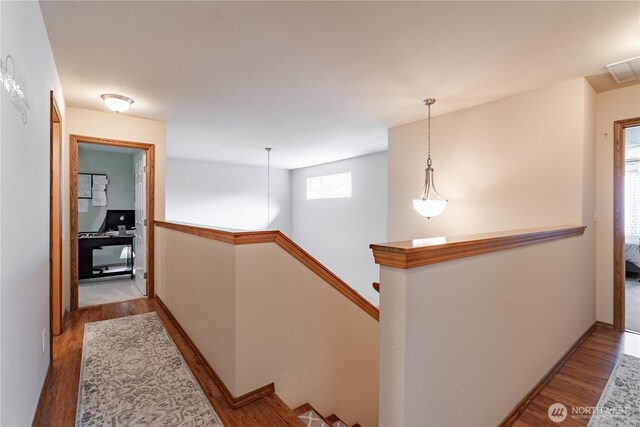 corridor featuring visible vents, an upstairs landing, and wood finished floors