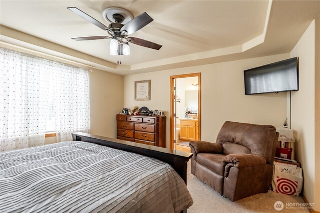 bedroom with connected bathroom, a raised ceiling, light carpet, and a ceiling fan