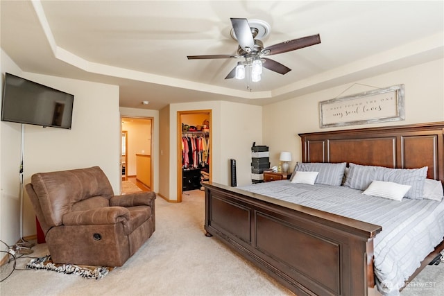 bedroom featuring a ceiling fan, a closet, light carpet, a walk in closet, and a raised ceiling