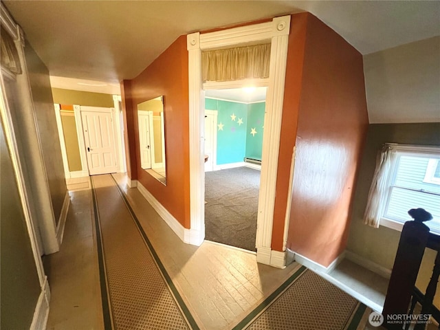 corridor with vaulted ceiling, baseboard heating, carpet, and baseboards