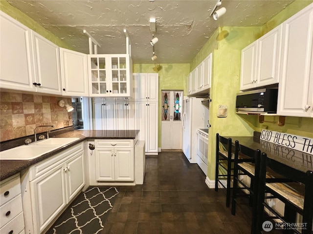 kitchen with a peninsula, white appliances, a sink, white cabinets, and dark countertops