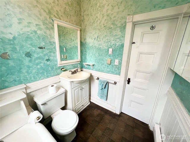 bathroom with a wainscoted wall, vanity, toilet, and wallpapered walls