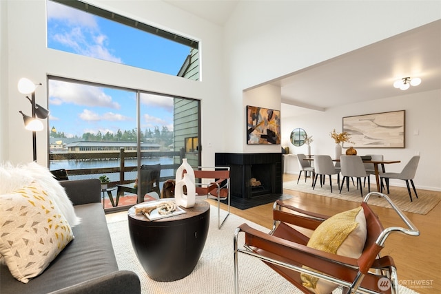 living room with a water view, a high ceiling, a multi sided fireplace, wood finished floors, and baseboards