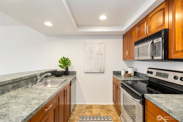 kitchen featuring a sink, baseboards, appliances with stainless steel finishes, a tray ceiling, and brown cabinetry