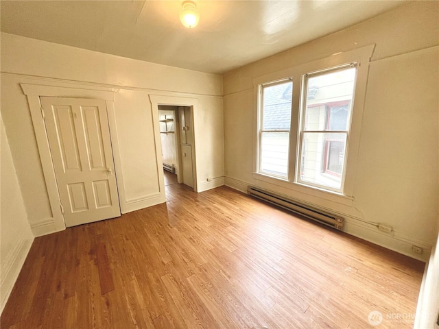 unfurnished room with a baseboard heating unit, baseboards, and wood finished floors