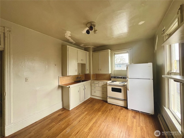 kitchen featuring white appliances, baseboards, a sink, and light wood finished floors