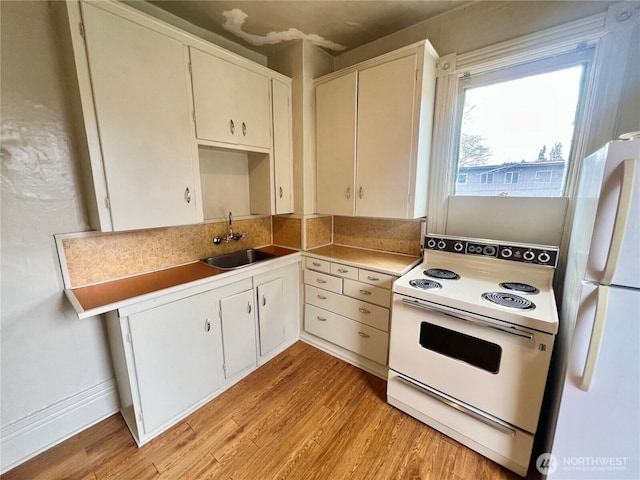 kitchen with light countertops, white appliances, a sink, and light wood-style floors