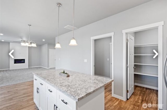 kitchen featuring decorative light fixtures, a glass covered fireplace, visible vents, and white cabinets