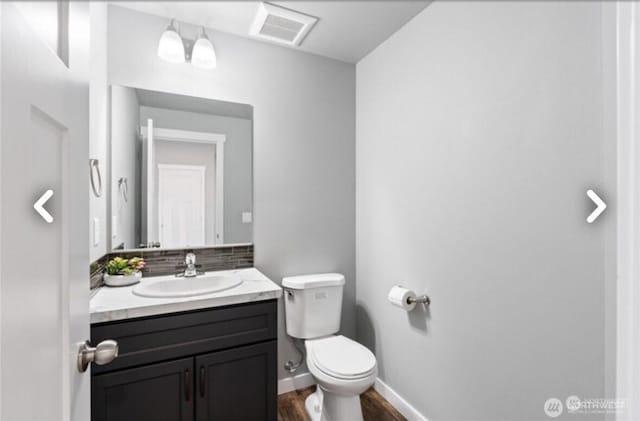 half bath with visible vents, toilet, vanity, wood finished floors, and baseboards