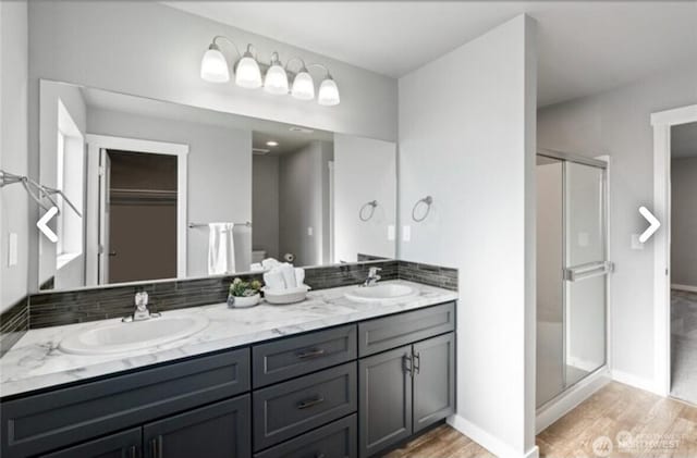 bathroom featuring double vanity, wood finished floors, a stall shower, and a sink