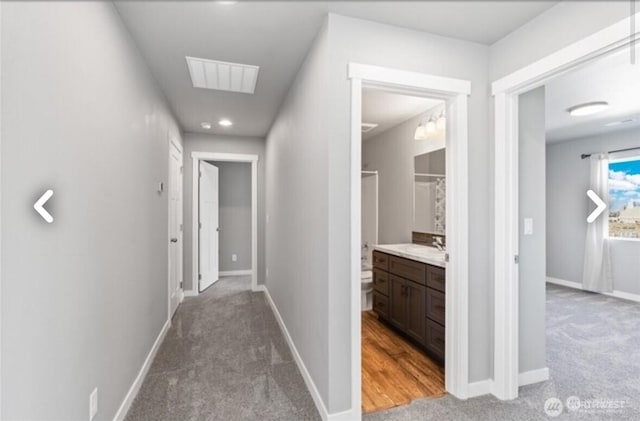 hallway with light carpet, baseboards, visible vents, and a sink