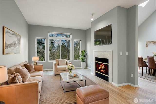 living room with light wood-type flooring, baseboards, and a glass covered fireplace