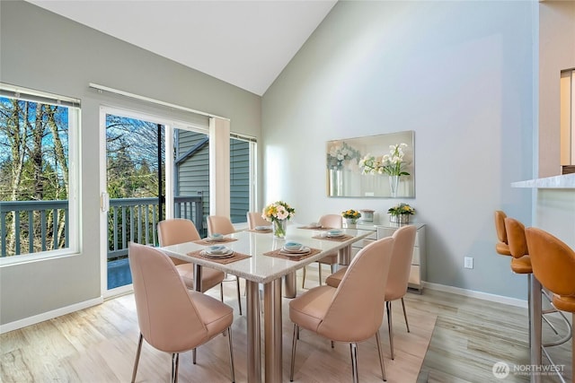 dining room featuring high vaulted ceiling, baseboards, and light wood finished floors