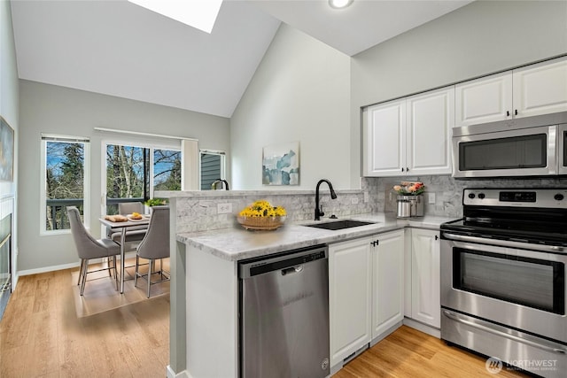 kitchen with a peninsula, a sink, white cabinetry, appliances with stainless steel finishes, and tasteful backsplash