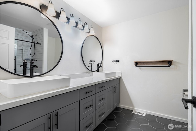 bathroom featuring tile patterned floors, a sink, a tile shower, and double vanity