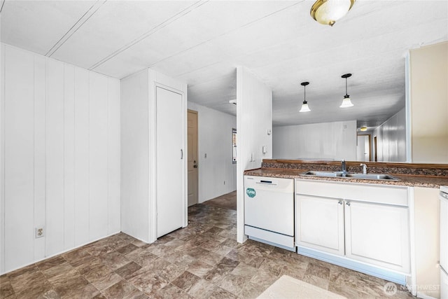 kitchen featuring wood walls, a sink, dishwasher, dark countertops, and pendant lighting