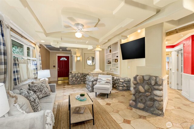 living room featuring lofted ceiling, a decorative wall, wainscoting, ceiling fan, and ornate columns