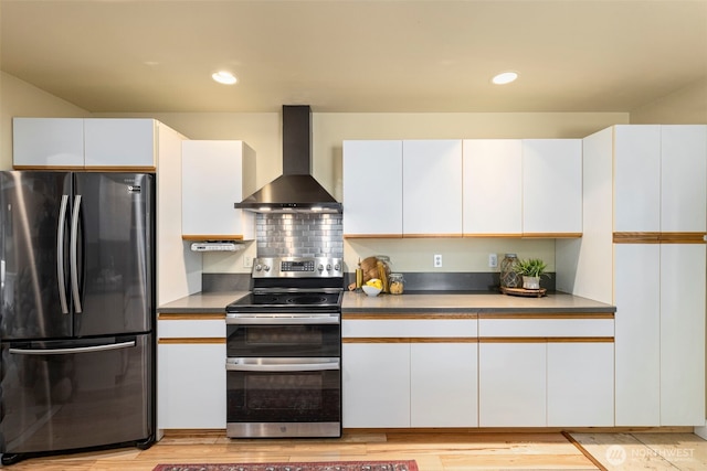 kitchen with light wood finished floors, white cabinets, freestanding refrigerator, wall chimney range hood, and double oven range