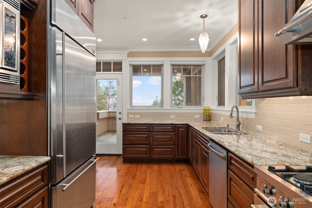 kitchen featuring built in appliances, under cabinet range hood, a sink, ornamental molding, and decorative backsplash