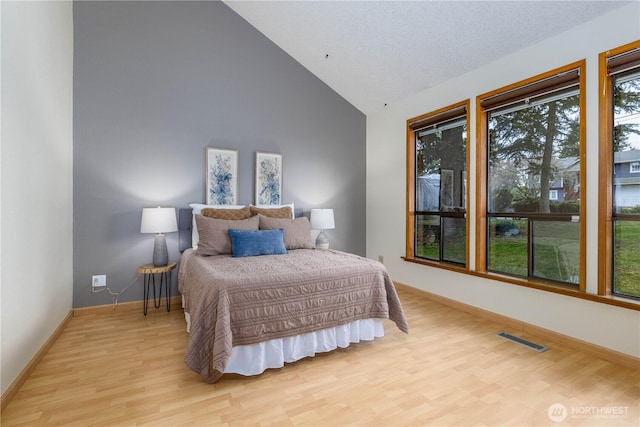 bedroom with high vaulted ceiling, visible vents, light wood-style flooring, and baseboards