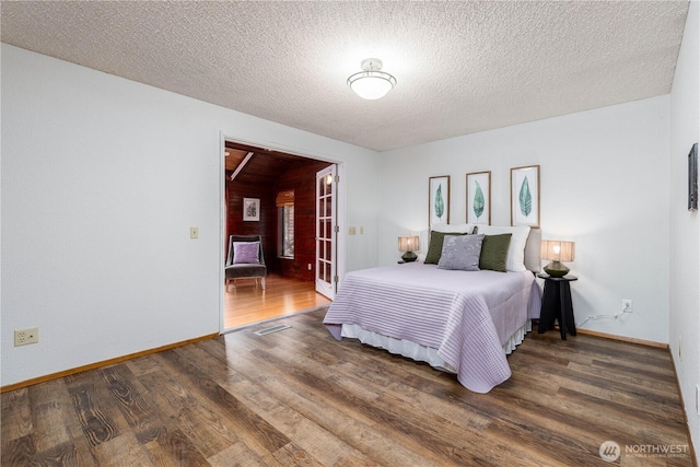 bedroom featuring visible vents, a textured ceiling, baseboards, and wood finished floors