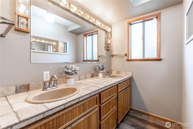 bathroom featuring double vanity, wood finished floors, a sink, and baseboards