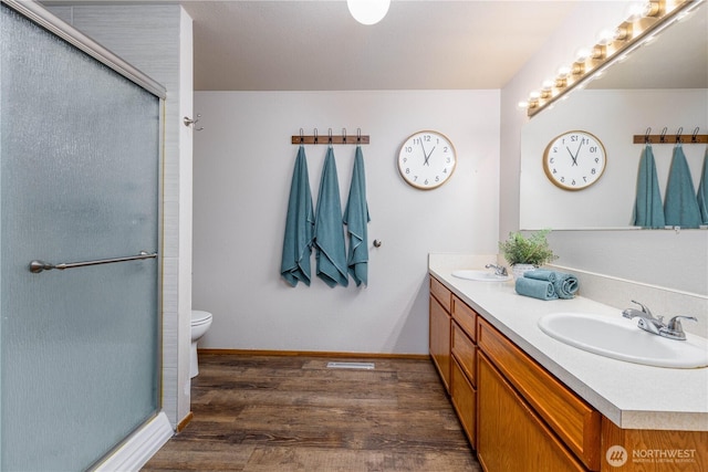 bathroom featuring double vanity, wood finished floors, a stall shower, and a sink