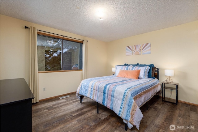 bedroom featuring visible vents, a textured ceiling, baseboards, and wood finished floors